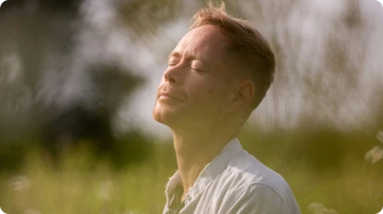 man with closed eyes in a field with head tilted towards the sky